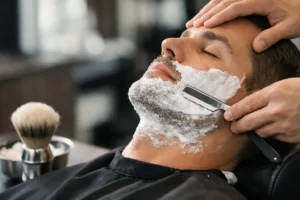 Barber using a straight razor on a man's lathered cheek.